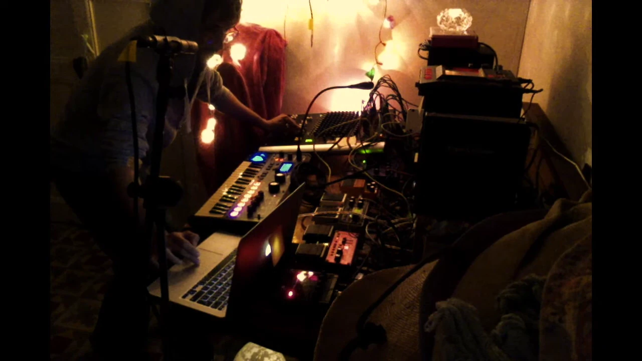 Video still of a home ambient setup with synths, mixer, pedals, and fairy lights